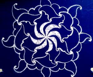 White swirling flower- a freehand rangoli with kolamavu on a blue plastic cover.